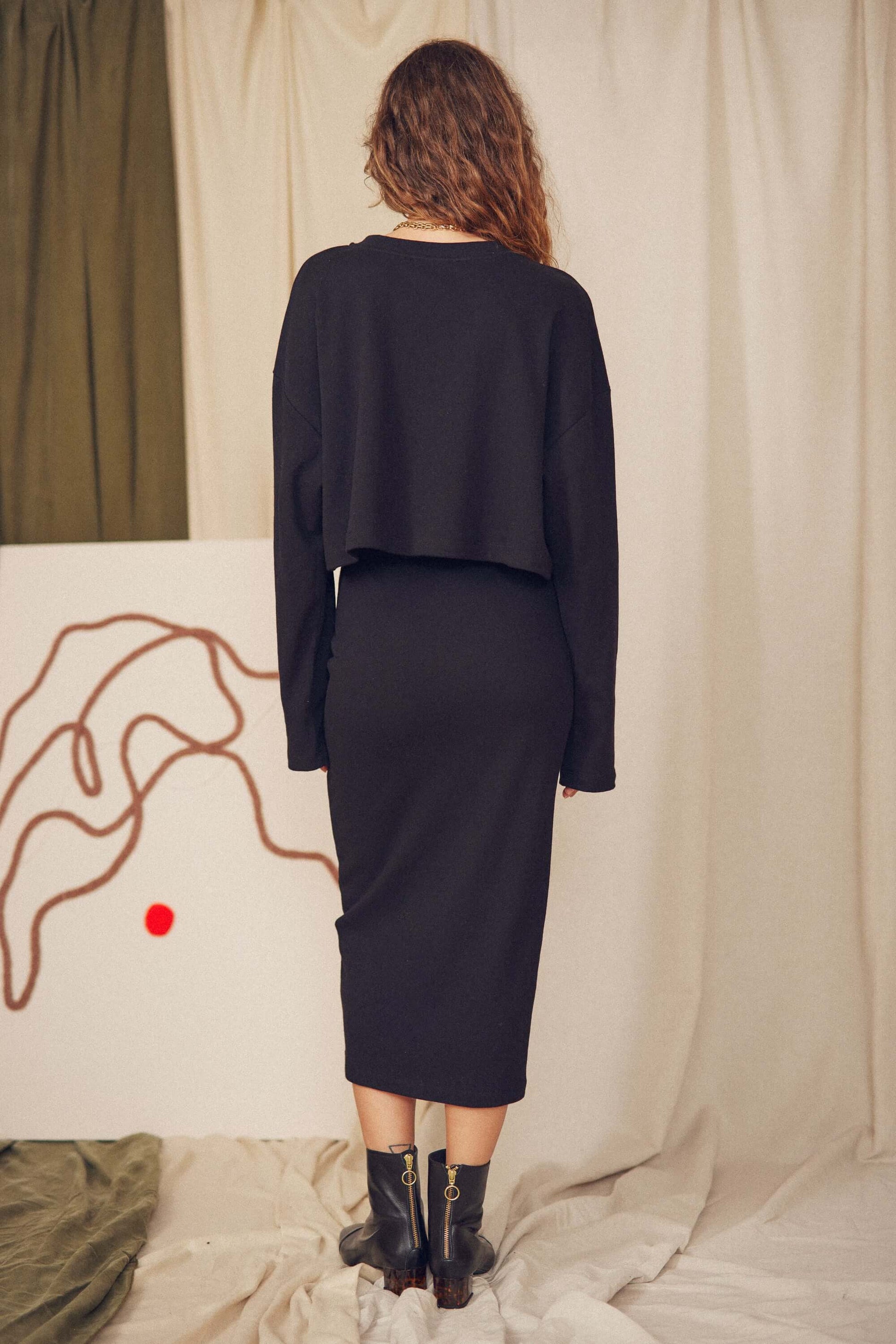 Woman wearing a black organic cotton midi skirt and cropped sweater, showcasing minimalist autumn/winter style.