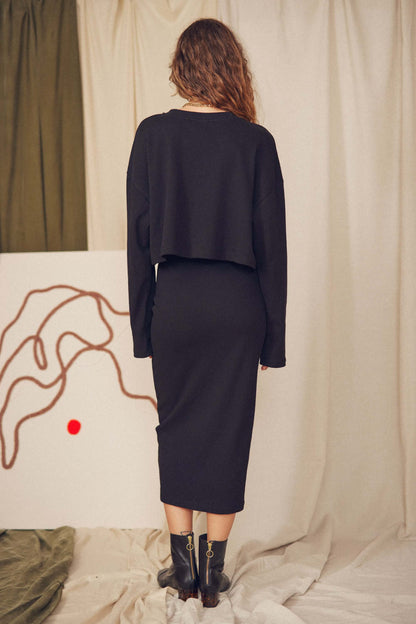 Woman wearing a black organic cotton midi skirt and cropped sweater, showcasing minimalist autumn/winter style.