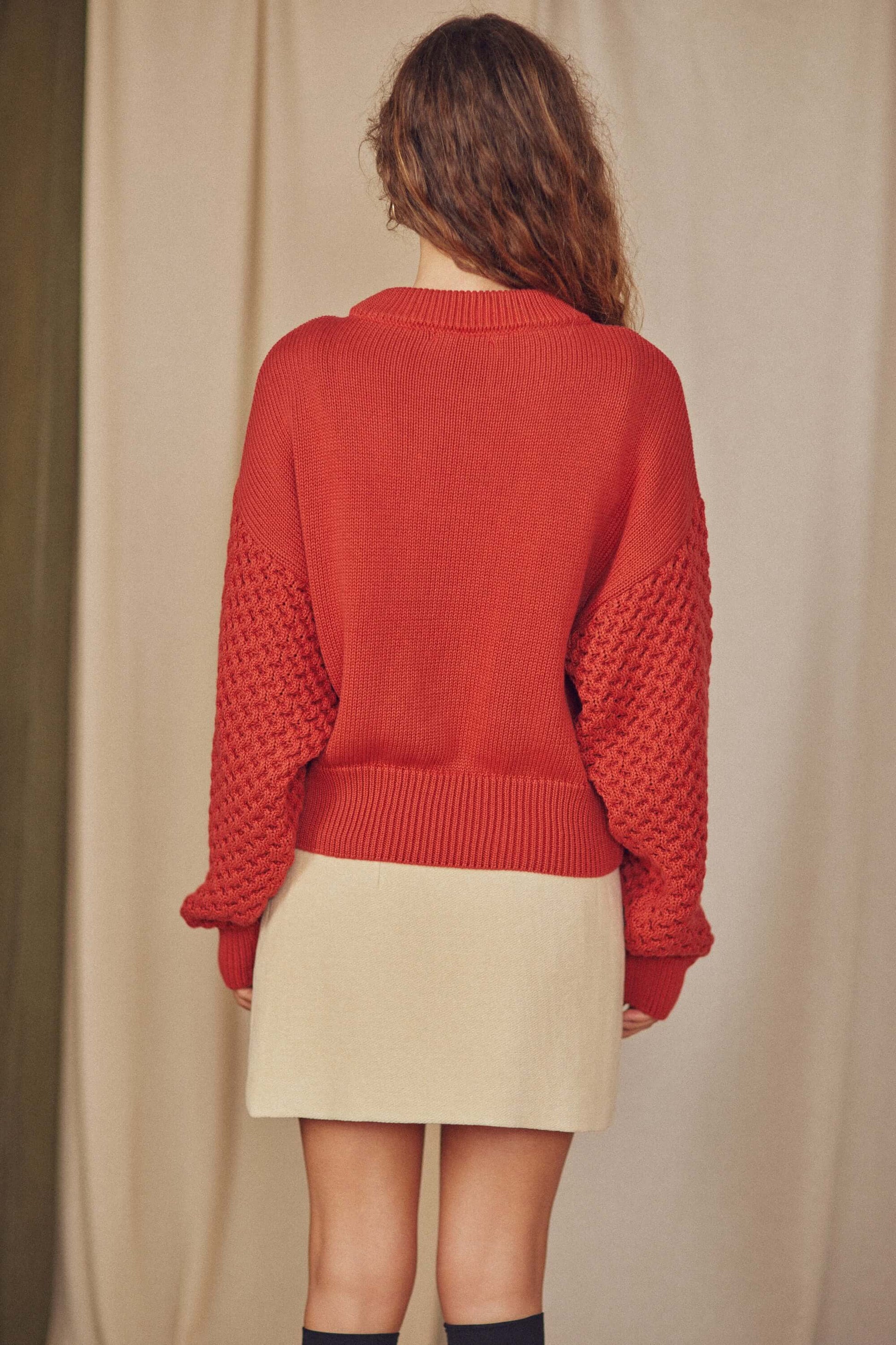 Back view of a woman wearing a Heavy Knit Rust Vegan Sweater with fantasy sleeves and neutral skirt.