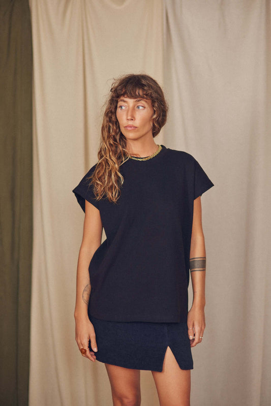 Model wearing a black organic cotton basic tee with short cap sleeves, styled with a dark skirt.