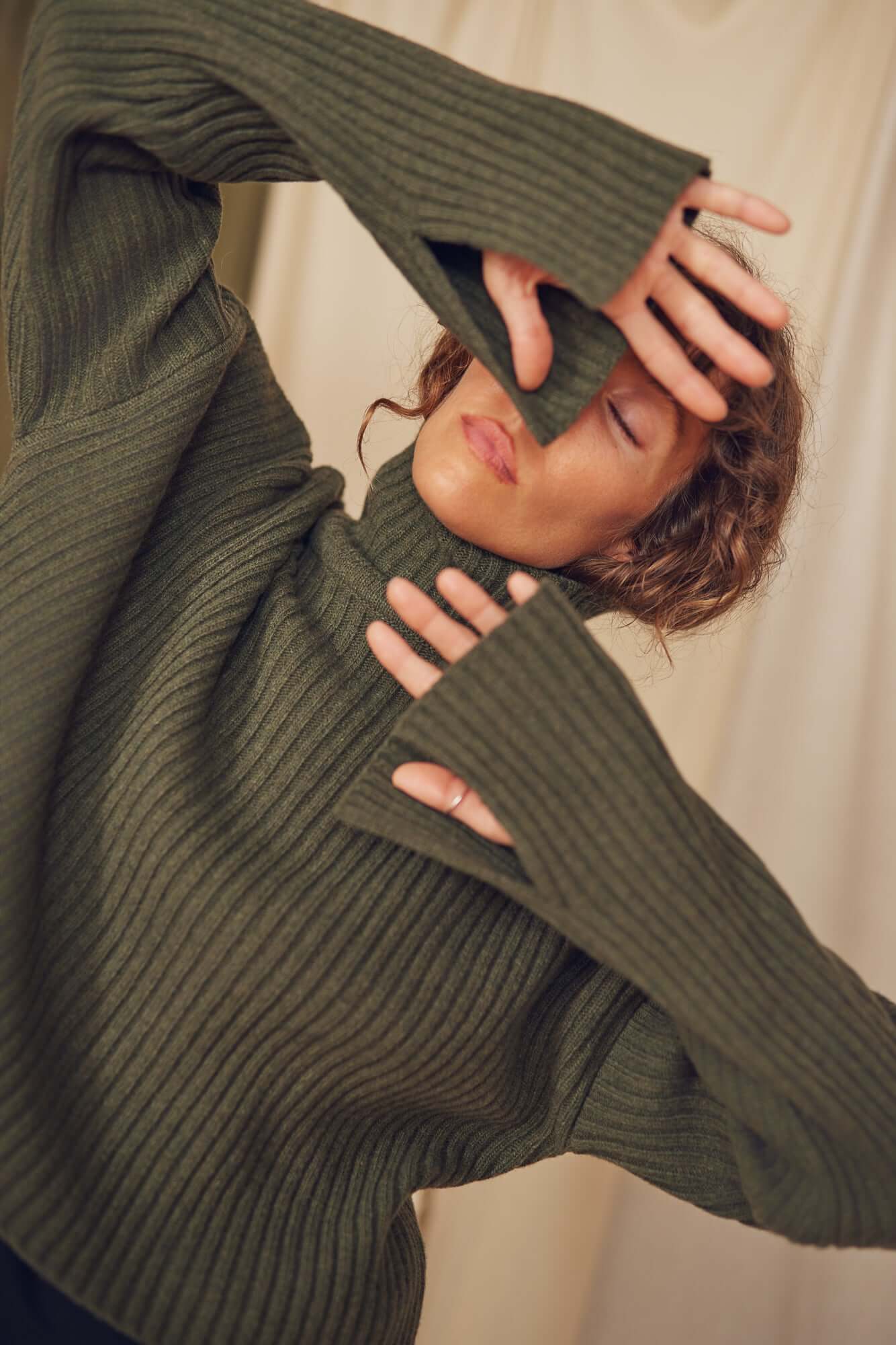 Woman wearing a khaki heavy knitted wool sweater with ribbed texture and sleeve split.