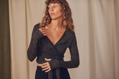 Woman wearing a black multiway recycled jersey wrap top with long sleeves and thumb holes, styled for autumn/winter.