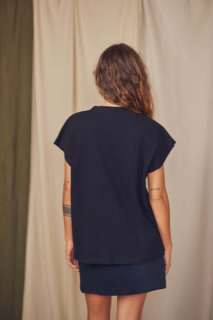 Back view of a woman wearing a black organic cotton tee with short cap sleeves, styled for autumn/winter.