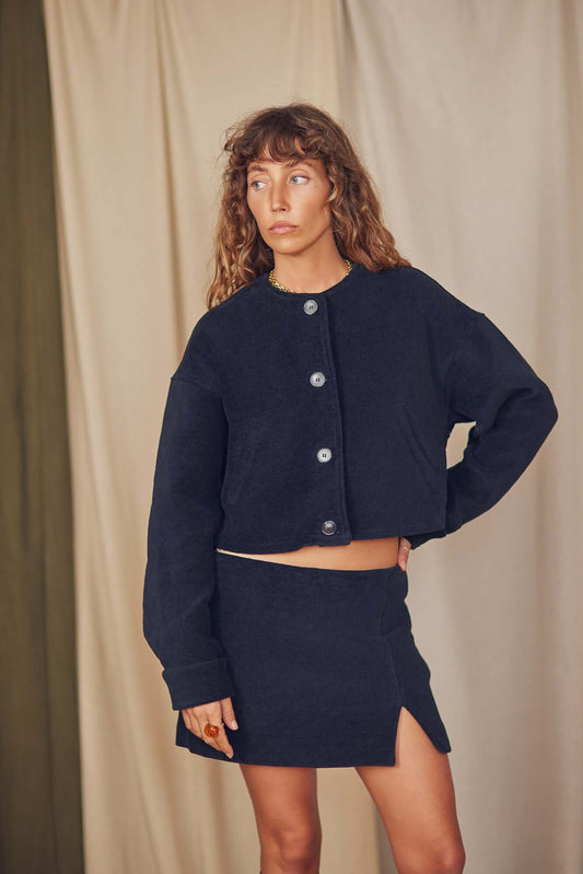 Model wearing a black organic cotton crop jacket with eco-friendly buttons, styled with a matching skirt.