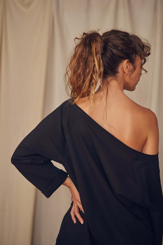 Woman wearing a black FLASHDANCE sweatshirt with an off the shoulder neckline, showcasing organic cotton material.