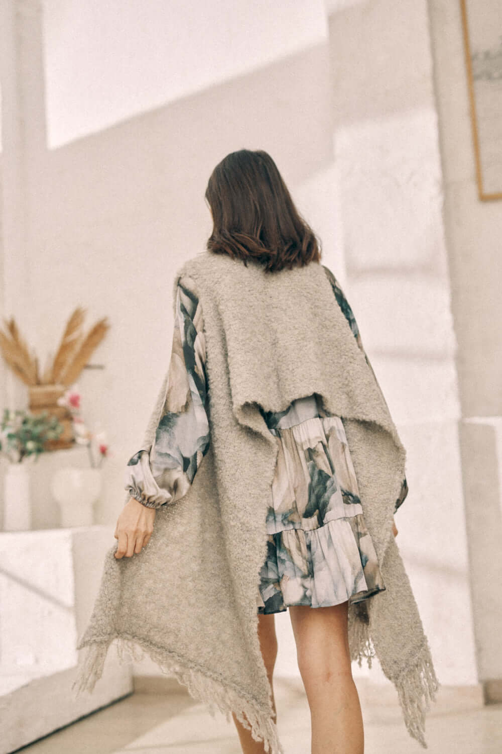 Woman wearing a versatile grey poncho scarf made from sustainable materials, styled as a poncho, paired with a floral dress.