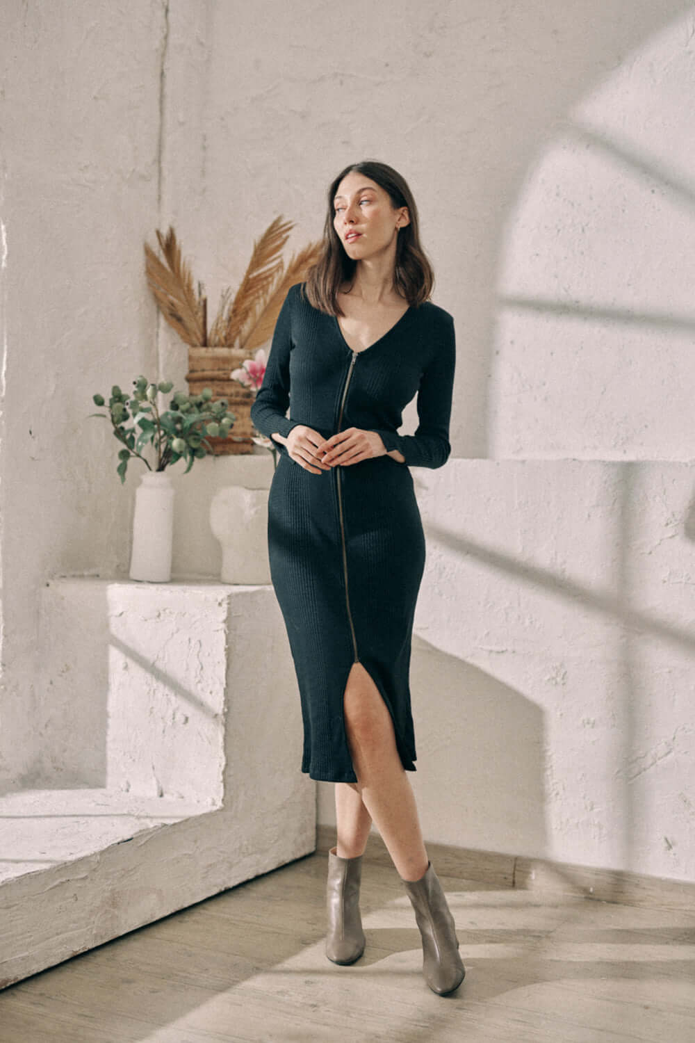 Woman wearing black reversible zip dress made from sustainable jersey with wrap front, posing in a sunlit room.