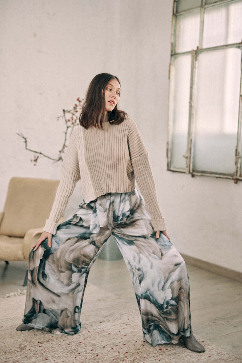 Woman wearing printed wide trousers in autumn print, made of 100% Ecovero viscose, with a ribbed sweater in a stylish interior.