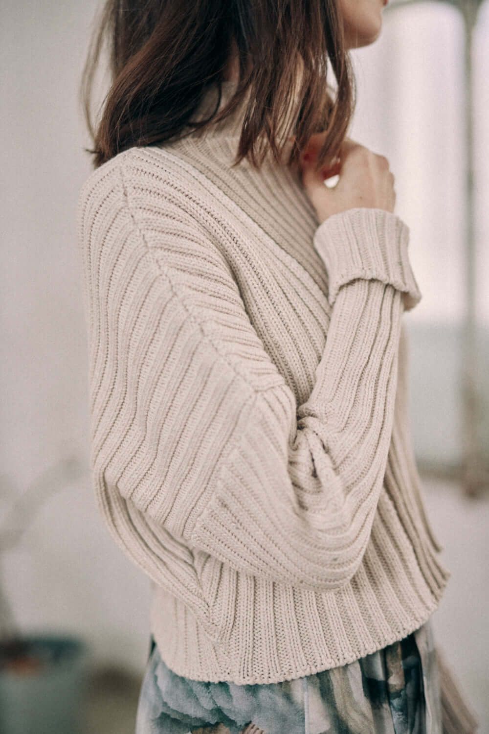 Woman wearing a bicolor beige sweater made of organic cotton with a high neck and wide fit. Cozy vegan fashion.