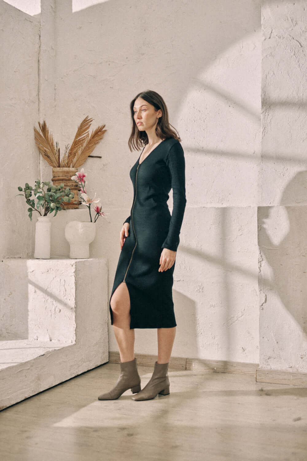 Woman wearing black reversible zip dress made of sustainable jersey, standing indoors in natural light.