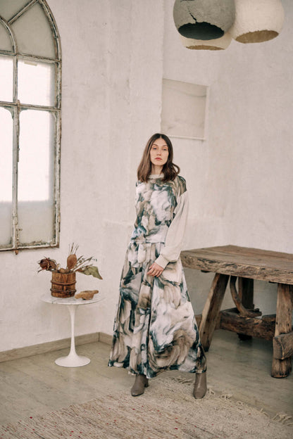 Woman wearing a printed reversible sweatshirt and skirt, standing in a rustic room with a wooden table and vintage window.