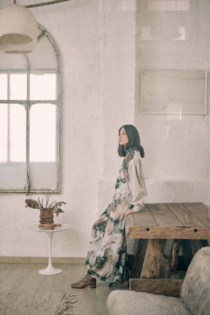 Woman in a printed reversible sweatshirt sitting in a rustic room with a wooden table and vintage window design.