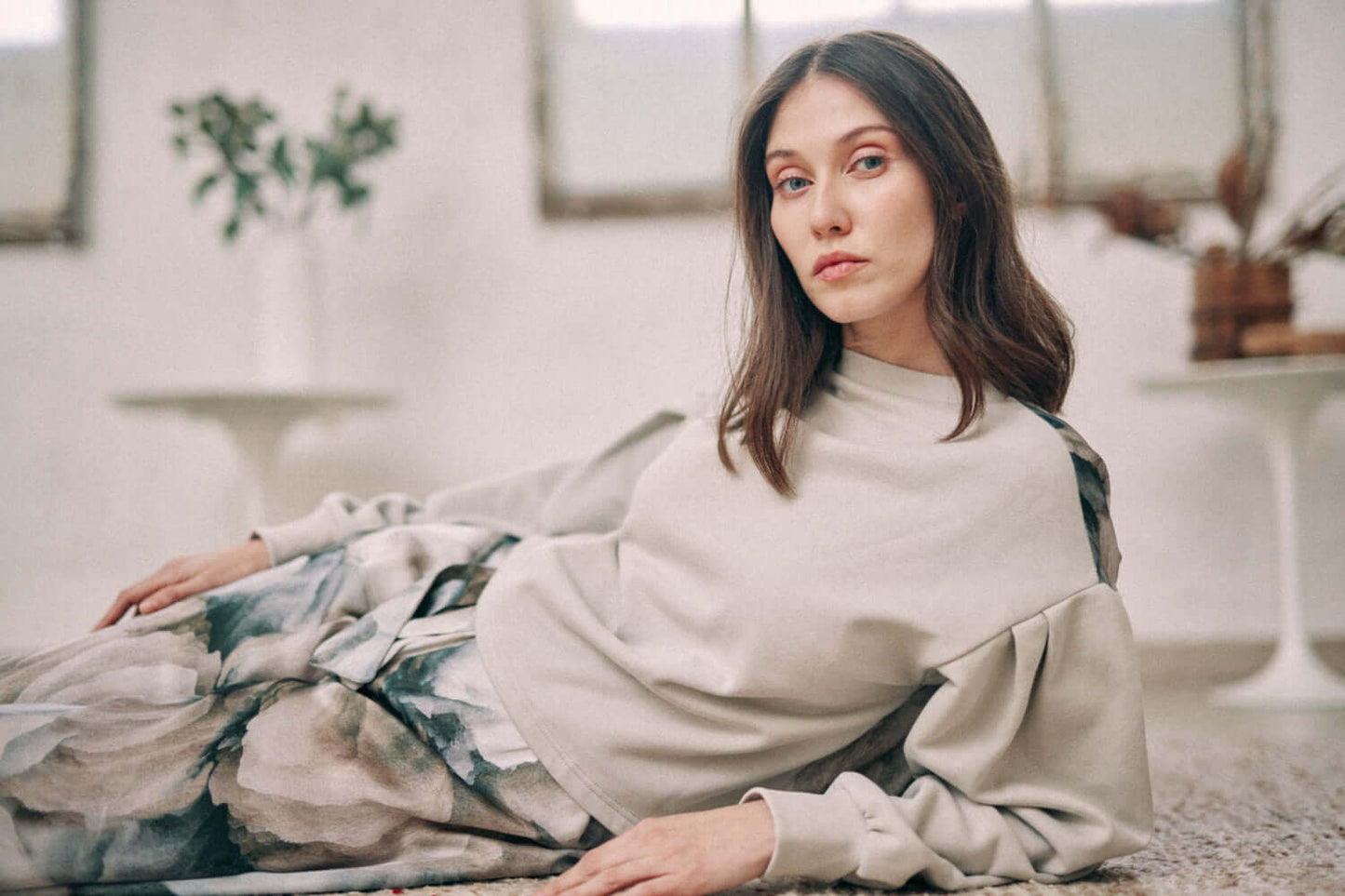 Woman wearing printed reversible sweatshirt in neutral tones, made from 100% Ecovero viscose, lying on a patterned surface.