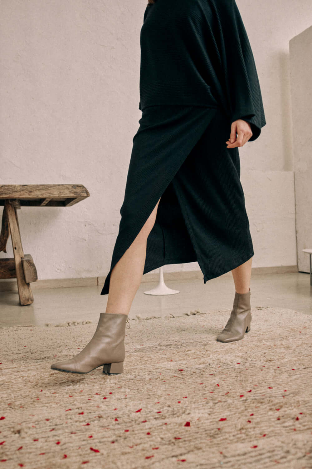 Black wrap skirt in thick jersey fabric, shown with a high slit, styled with ankle boots.