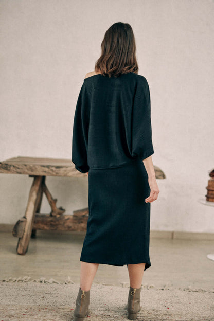 Woman modeling a versatile black wrap skirt made from recycled polyester and organic cotton jersey fabric, back view.