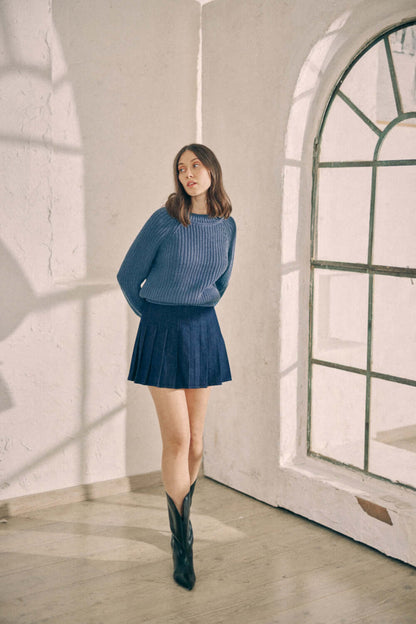 Woman wearing navy sweater and skirt in sunlit room, showcasing online exclusive made from organic cotton.