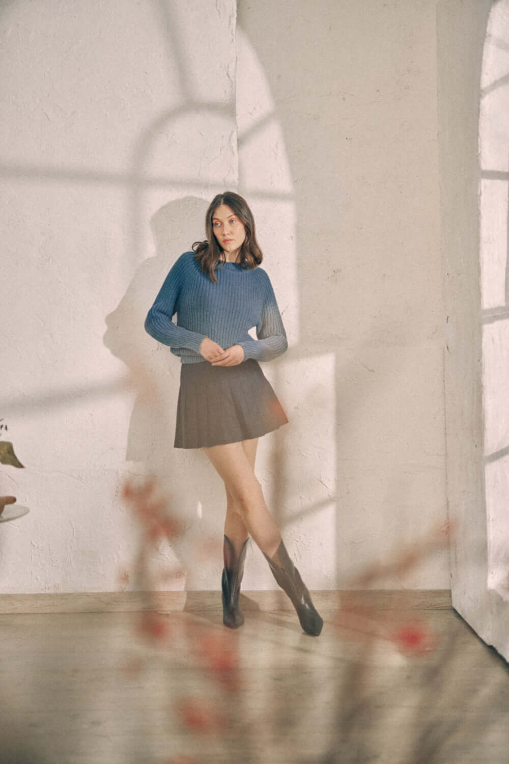 Woman wearing navy sweater and skirt in sunlit room.