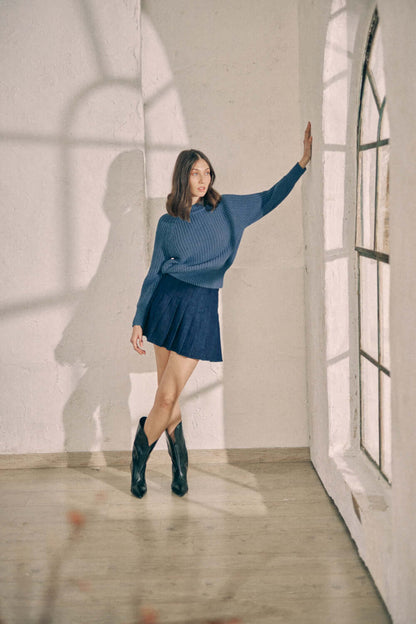 Woman wearing navy organic cotton sweater and skirt by window in bright room