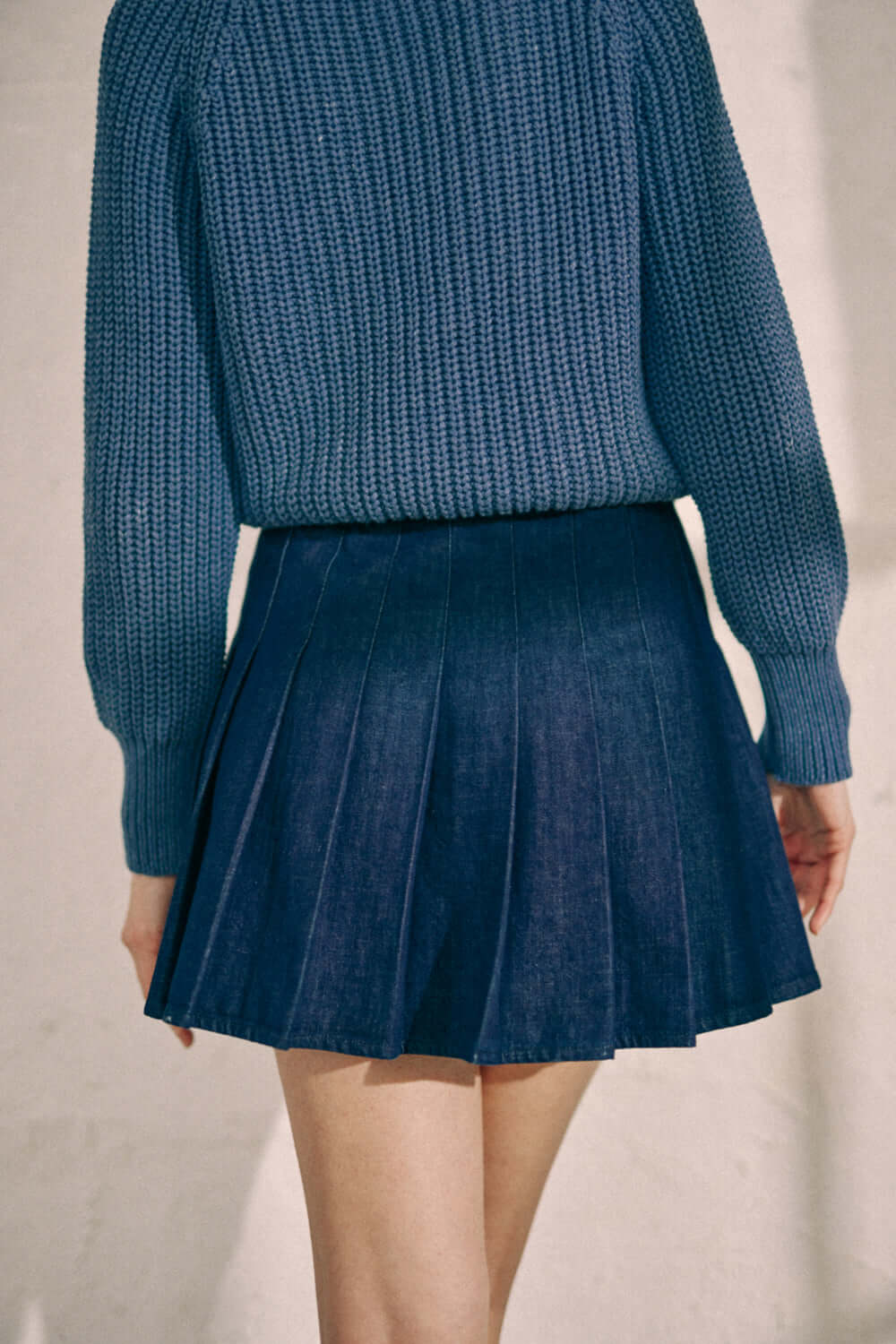 Navy denim pleated skirt in organic cotton, featuring a back metal zip, showcased by a model wearing a blue sweater.