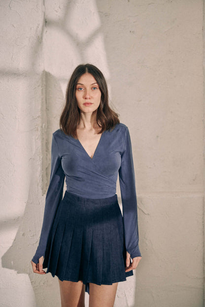 Woman wearing navy denim pleated skirt made from 100% organic cotton, styled for a modern preppy look.