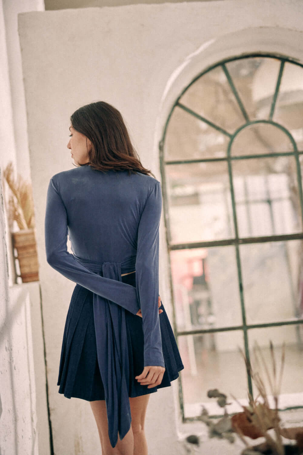 Woman wearing navy cupro wrap top with ties, shown from the back, stands in front of a glass window in a stylish indoor setting.