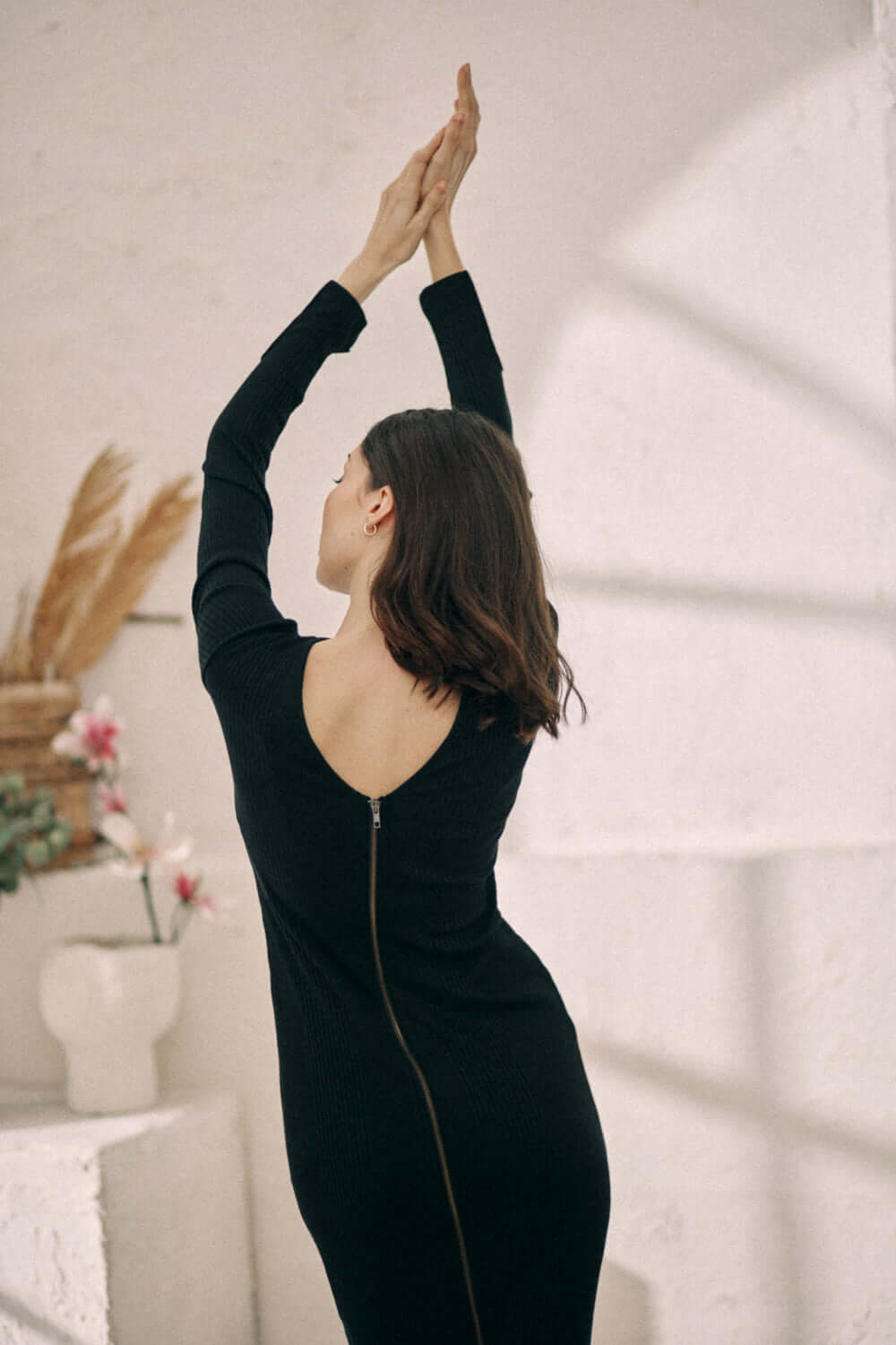 Woman wearing black reversible zip dress in sustainable thick jersey with arms raised, showcasing back zipper and wrap front design.