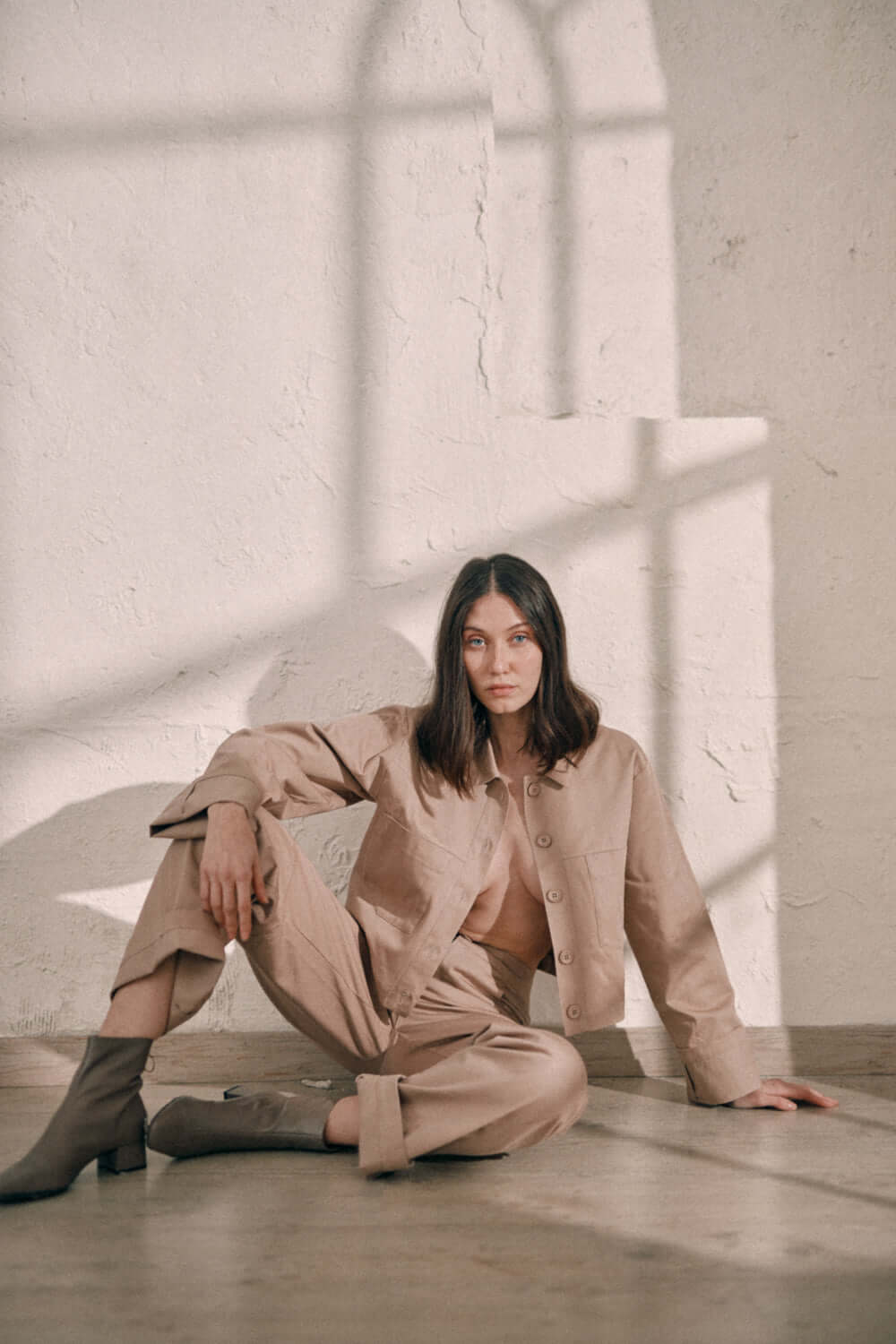 Model wearing taupe denim trousers and matching jacket in a minimalist setting.