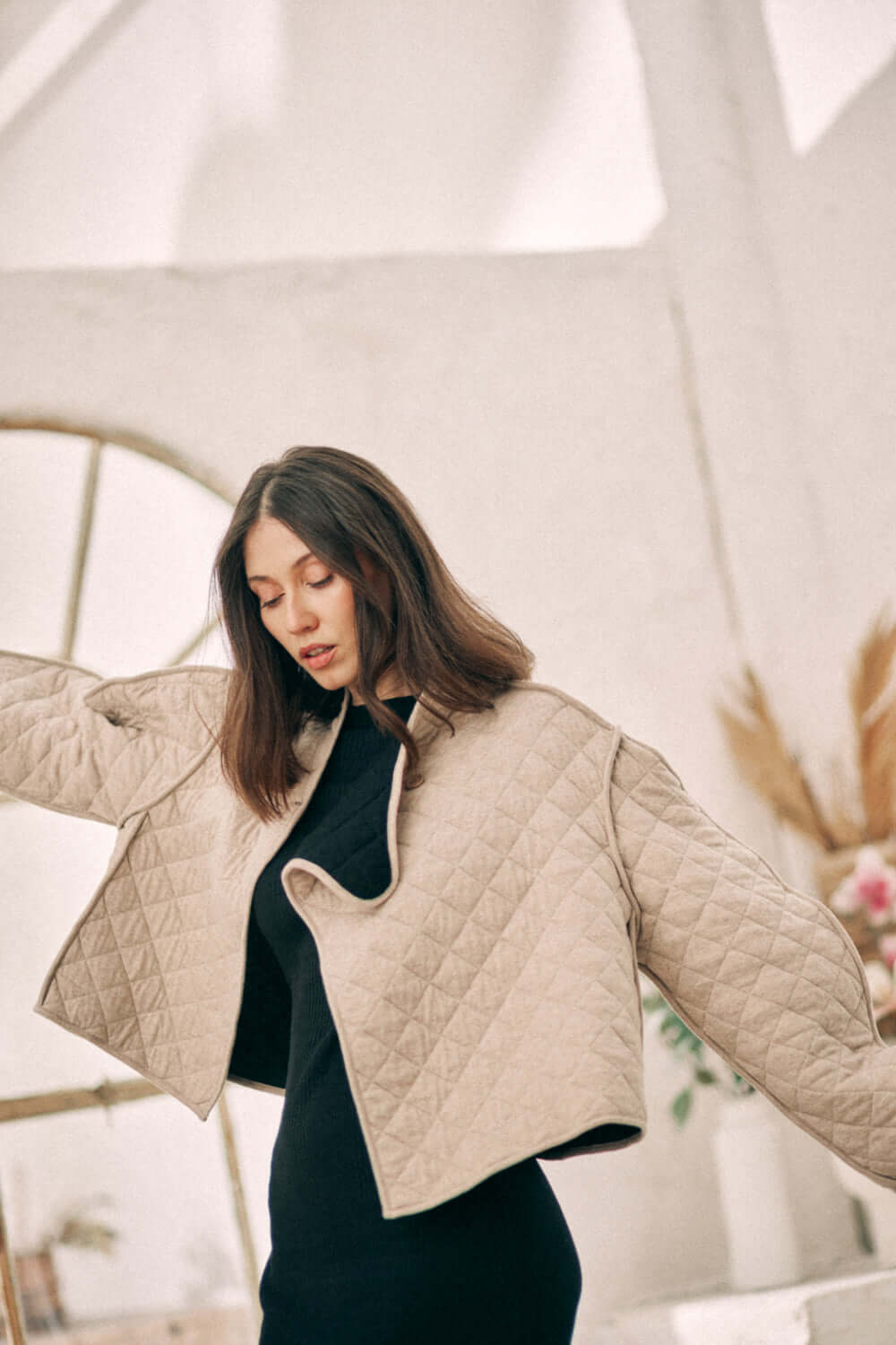 Woman wearing beige reversible padded jacket made from sustainable materials, posing in light-filled room.