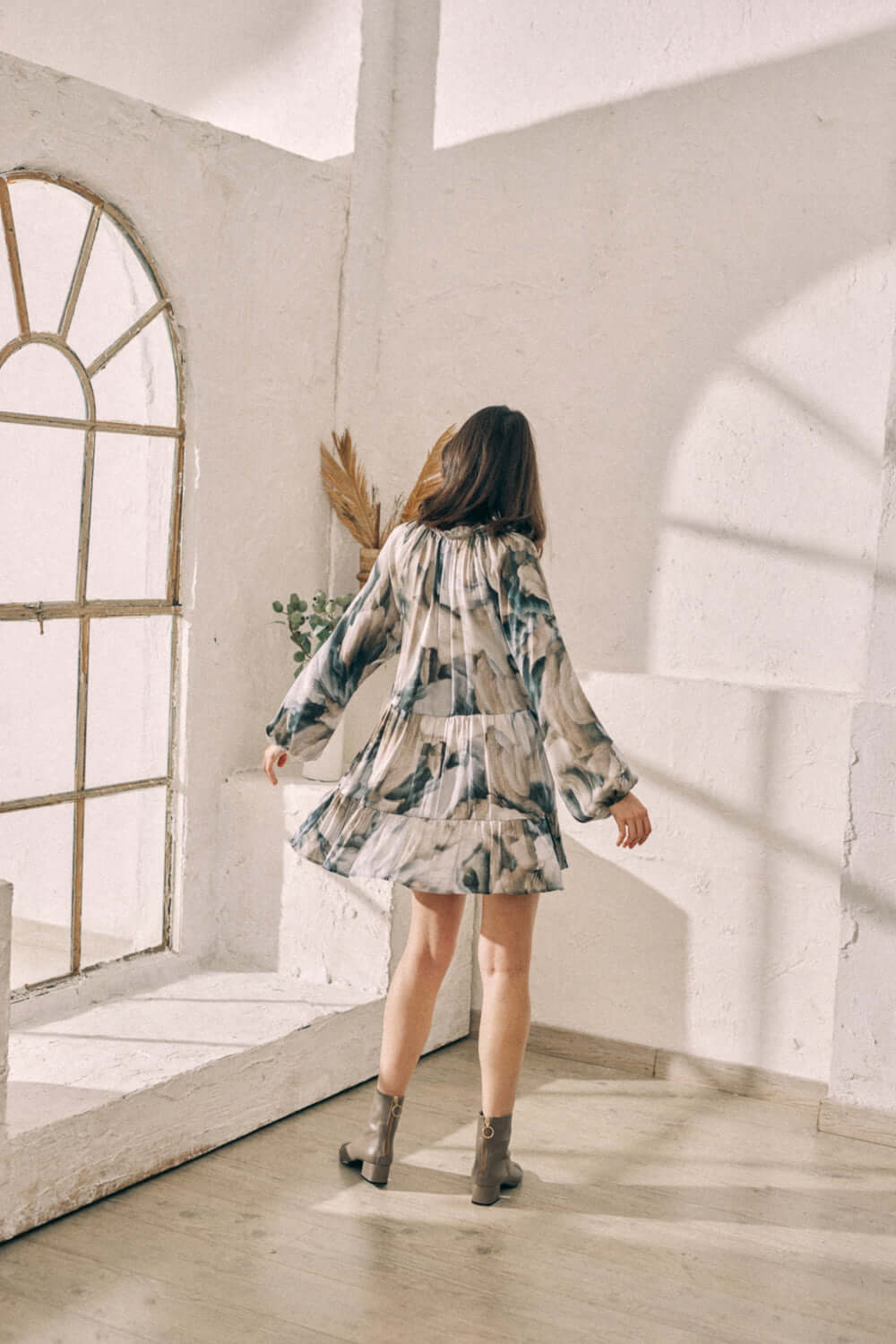 Woman wearing a flowy mini dress with Ecovero autumn print, showcasing the feminine frills and style in a sunlit room.