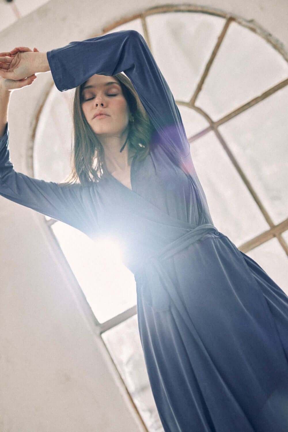 Woman wearing navy cupro wrap dress in front of an arched window