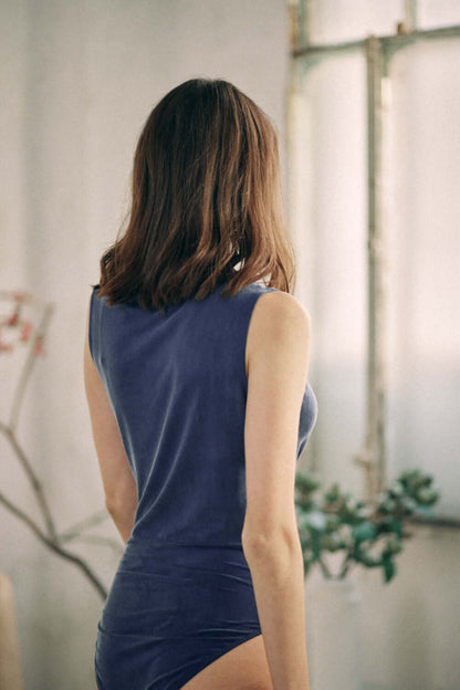 Woman wearing navy cupro bodysuit with velvety finish, back view, sleeveless design, perfect to pair with jeans.