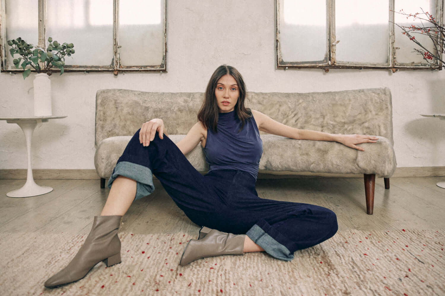 Woman wearing navy denim trousers made from organic cotton, seated on floor with ankles turned up, showcasing a stylish casual look.