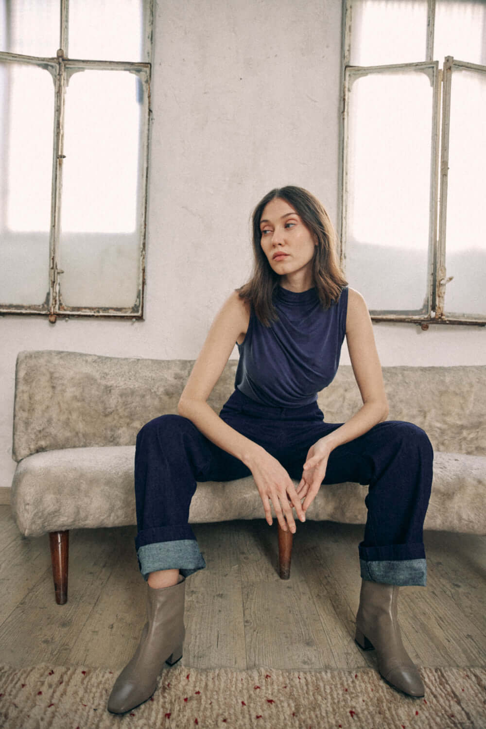 Woman wearing navy denim trousers with turned ankles, seated in a vintage setting.