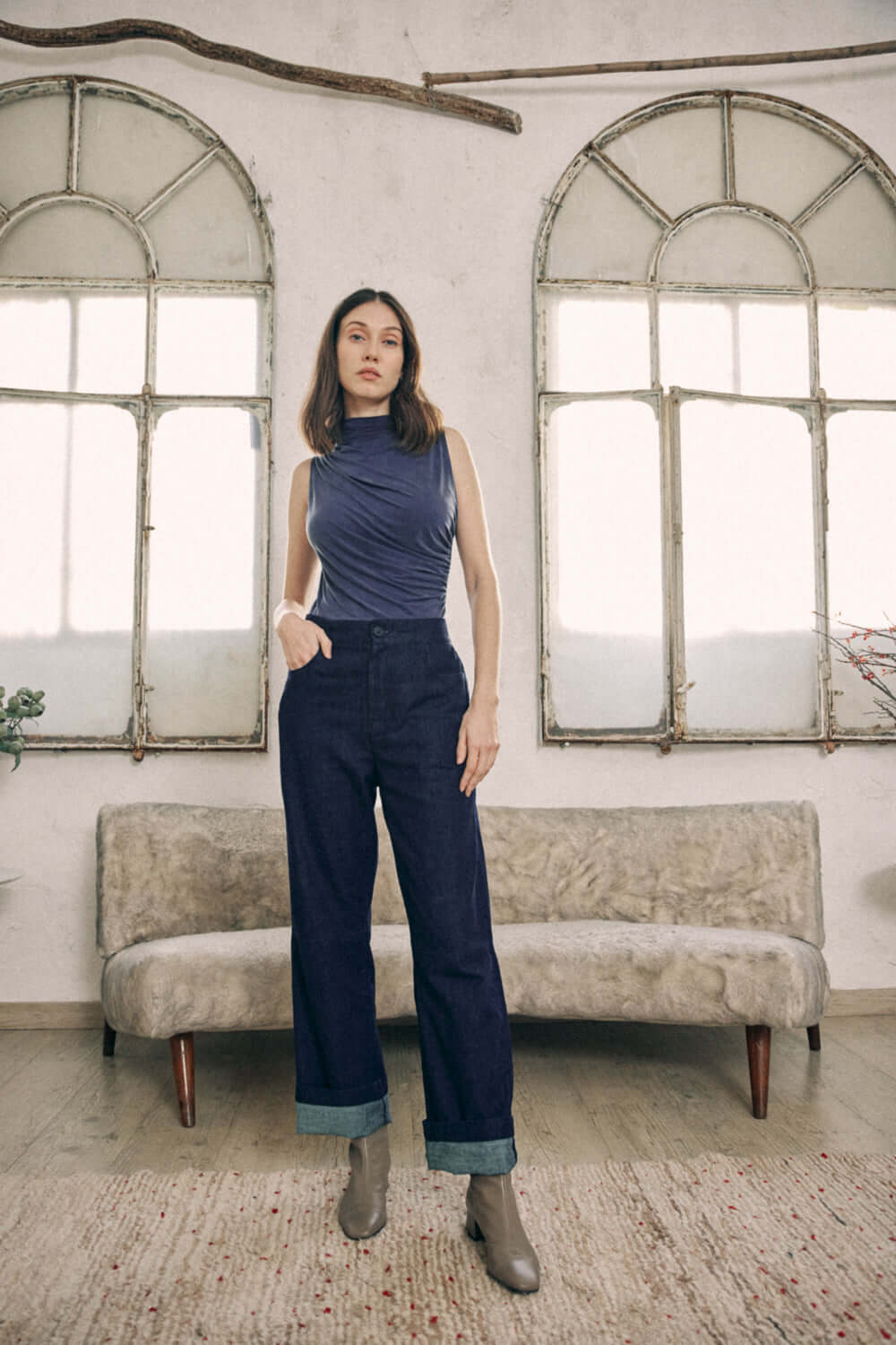 Woman wearing navy cupro bodysuit with drape detail bust, paired with high-waisted jeans in stylish indoor setting.