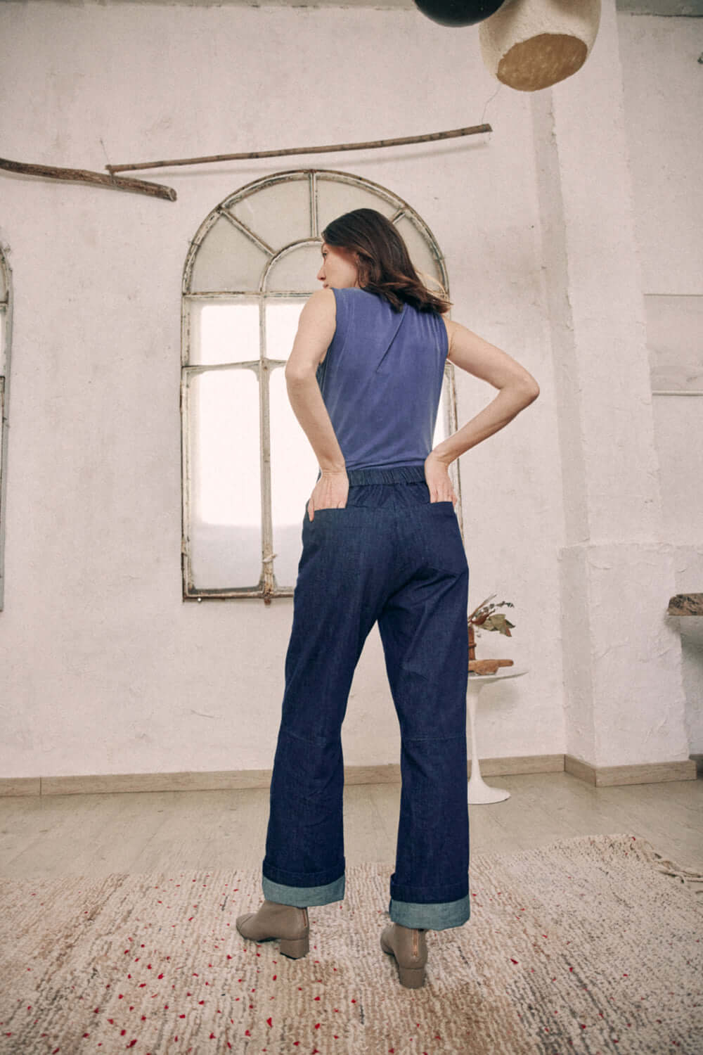 Back view of model wearing navy cupro bodysuit and rolled-up jeans in a rustic setting, highlighting the versatile style of the outfit.