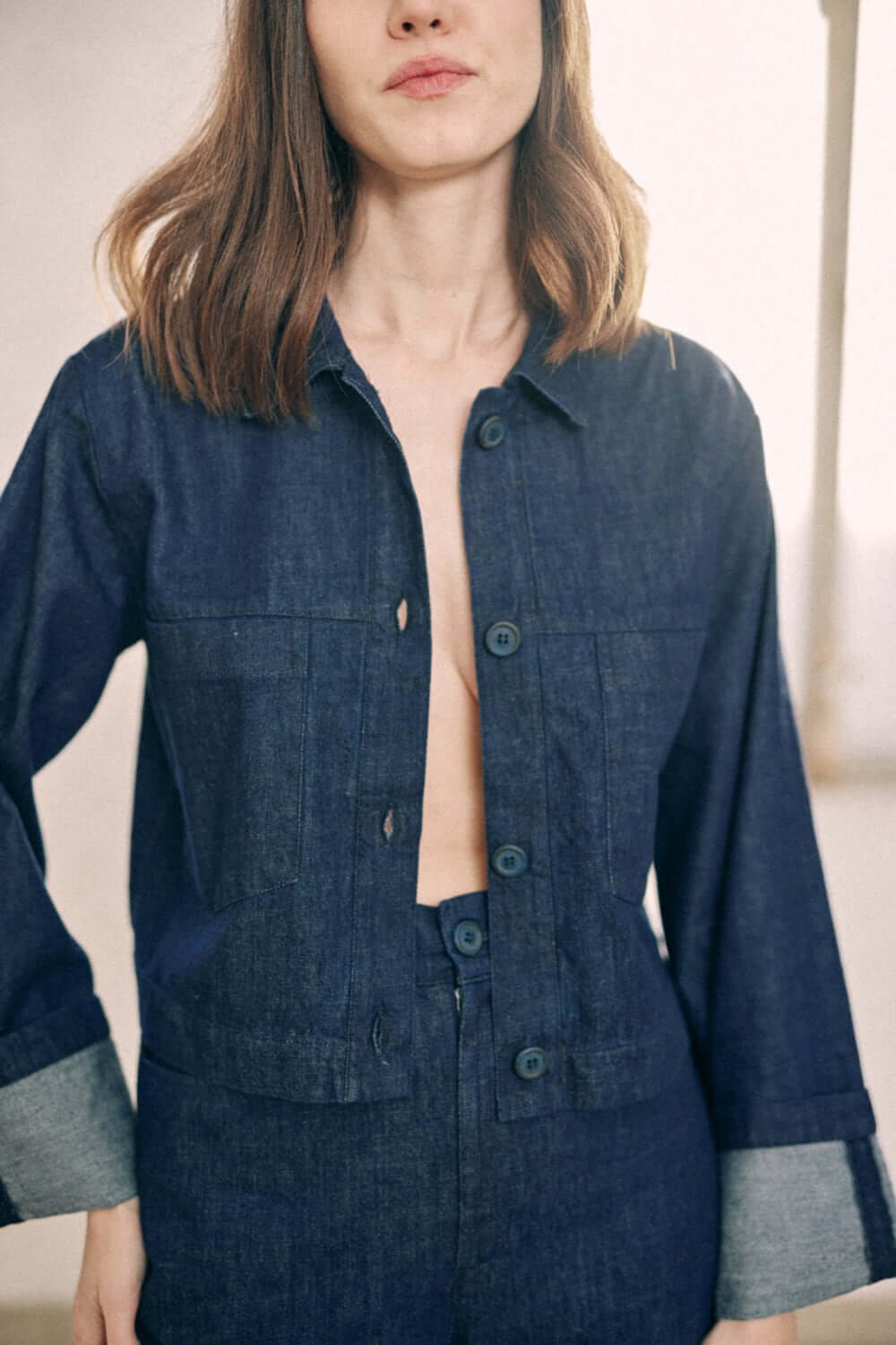 Woman wearing navy denim jacket with turned sleeves made from 100% organic cotton, showcasing COSSAC branded buttons.