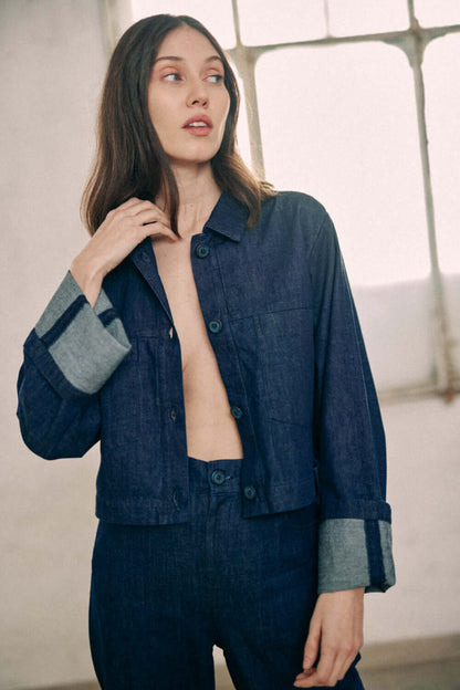 Woman modeling navy denim jacket made from 100% organic cotton, featuring turned-up sleeves and COSSAC buttons.