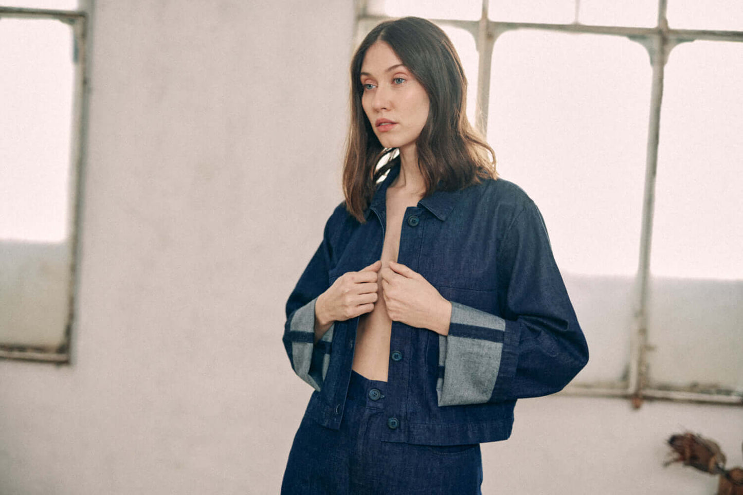 Woman wearing navy denim jacket with turned sleeves made of 100% organic cotton from Porto, customized buttons, and improved fit.