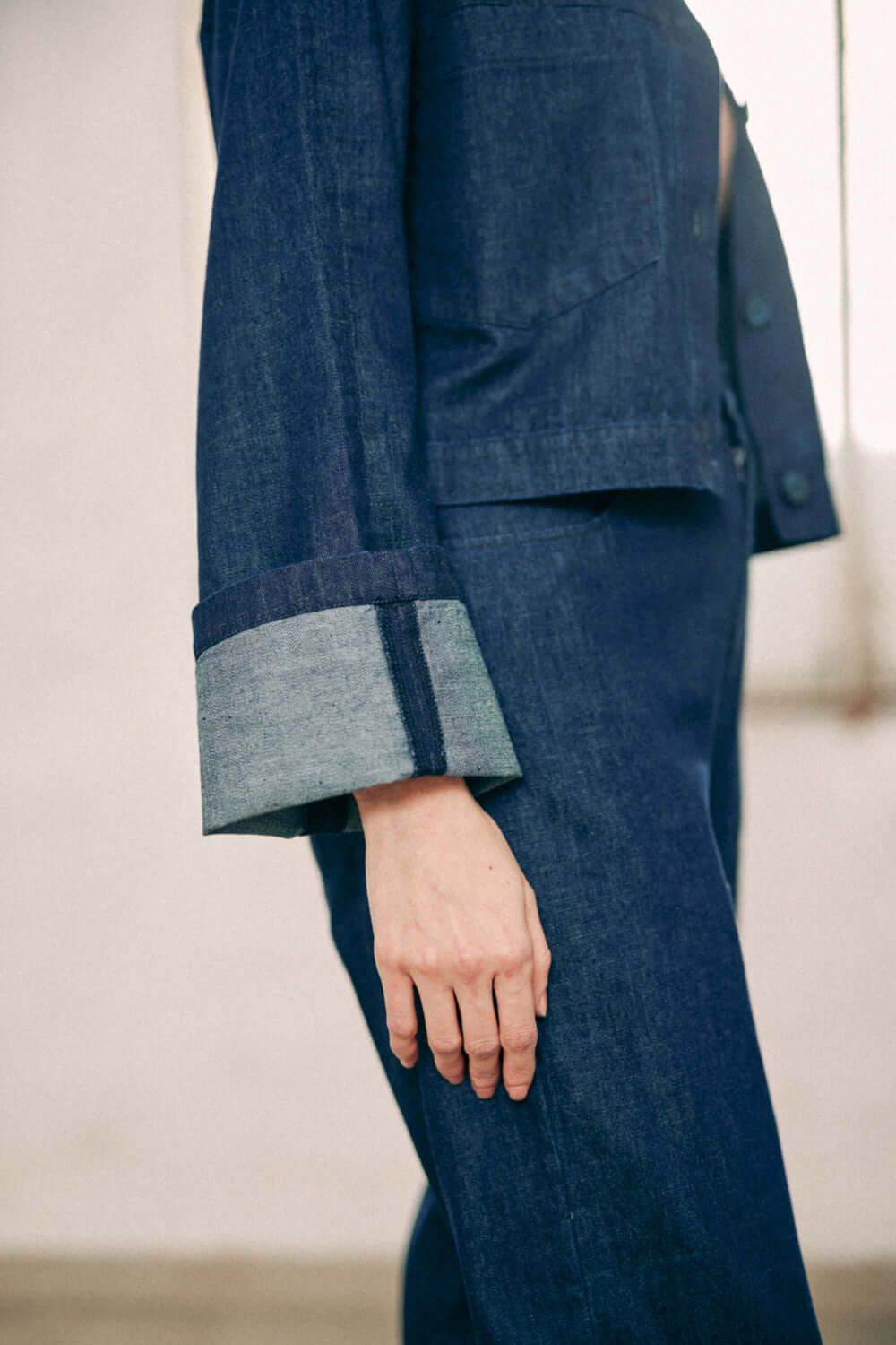 Close-up of navy denim trousers and jacket, made from 100% organic cotton, showing design details and turned ankle.