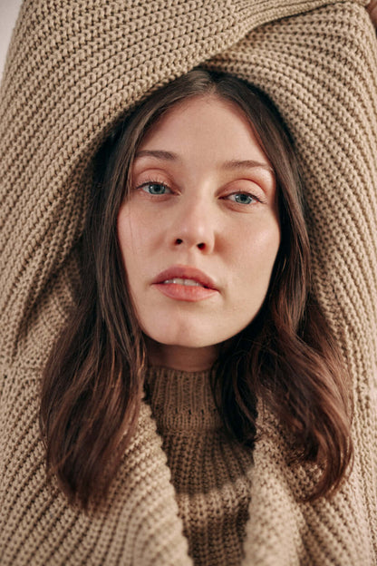 Woman wearing taupe sweater made from organic cotton, arms raised, showcasing crew neck design.