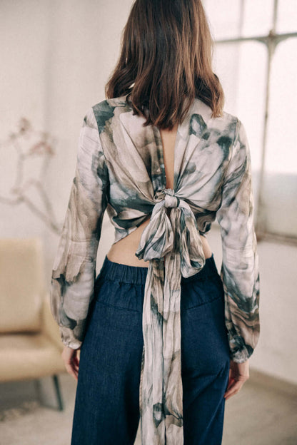 Woman wearing printed wrap top with back tie and long sleeves, showcasing autumn print design in soft indoor setting.