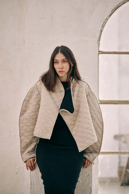 Woman wearing beige reversible padded jacket crafted from organic cotton and recycled polyester, styled in an indoor setting.