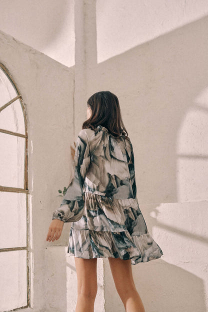 Woman wearing printed mini dress with flowy frills and autumn Ecovero print in bright, sunlit room. Sustainable fashion.