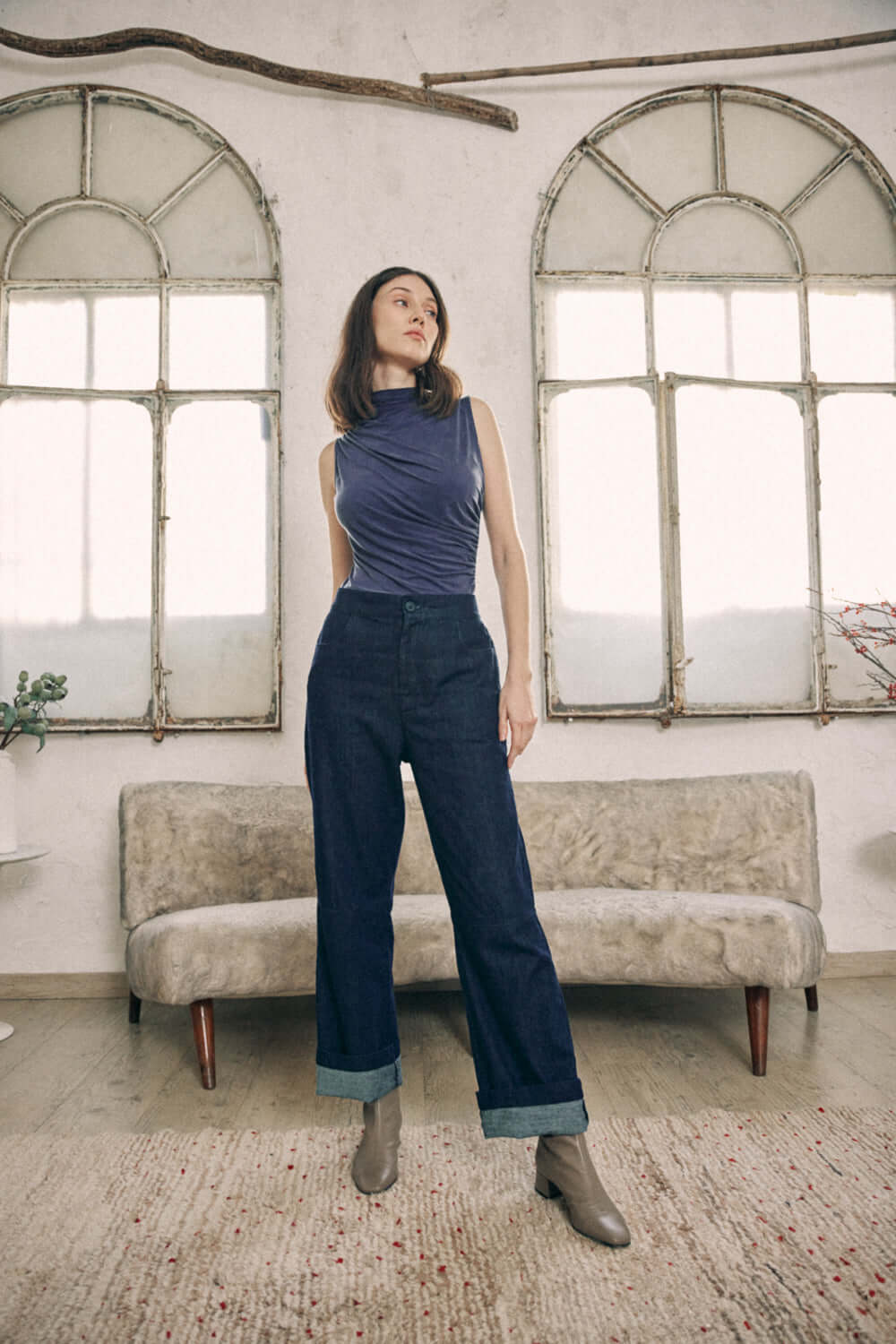 Woman wearing navy denim trousers made from organic cotton standing in front of antique windows, showcasing a classic yet modern style