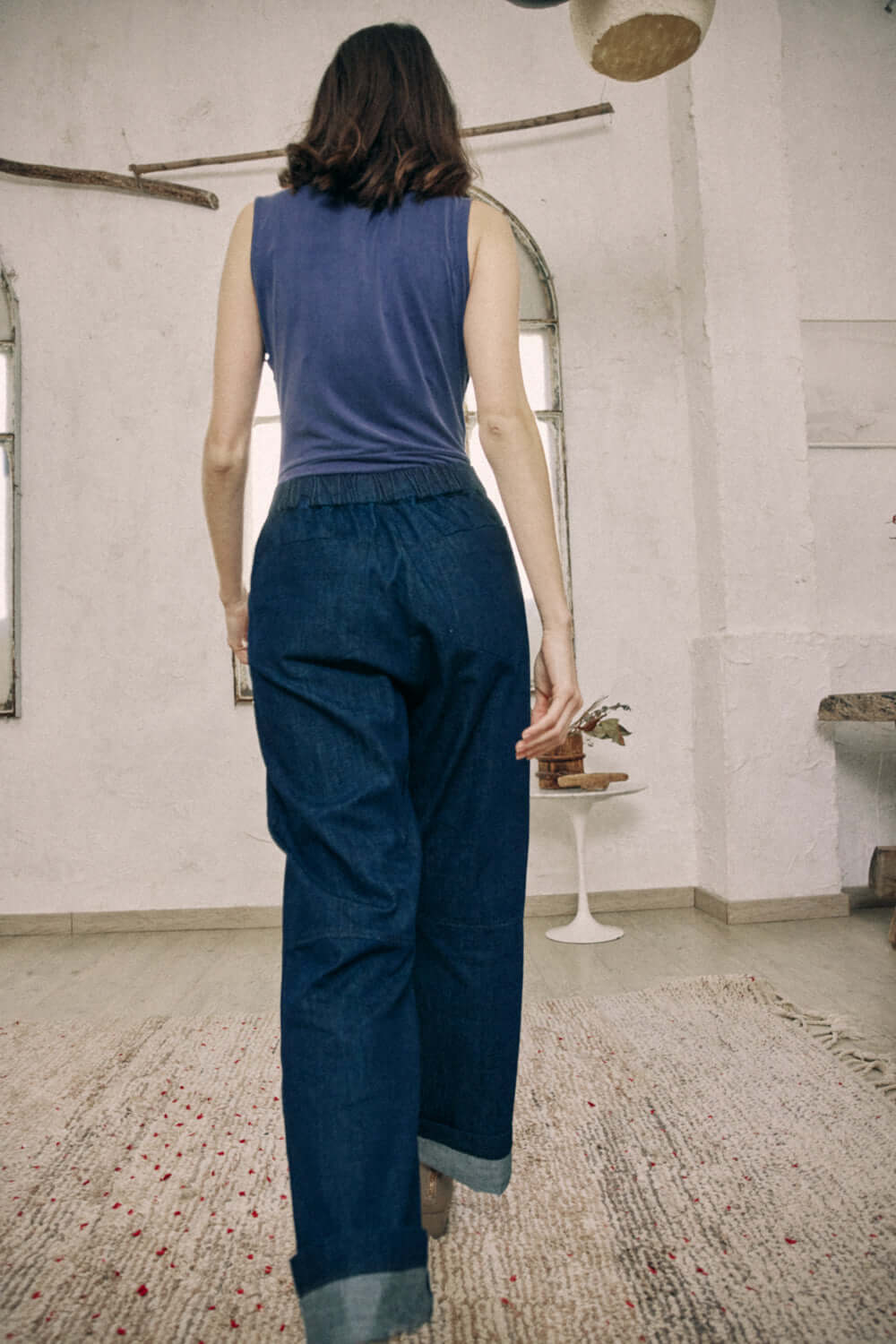 Model wearing navy denim trousers made from organic cotton, showcasing back details and turned ankles