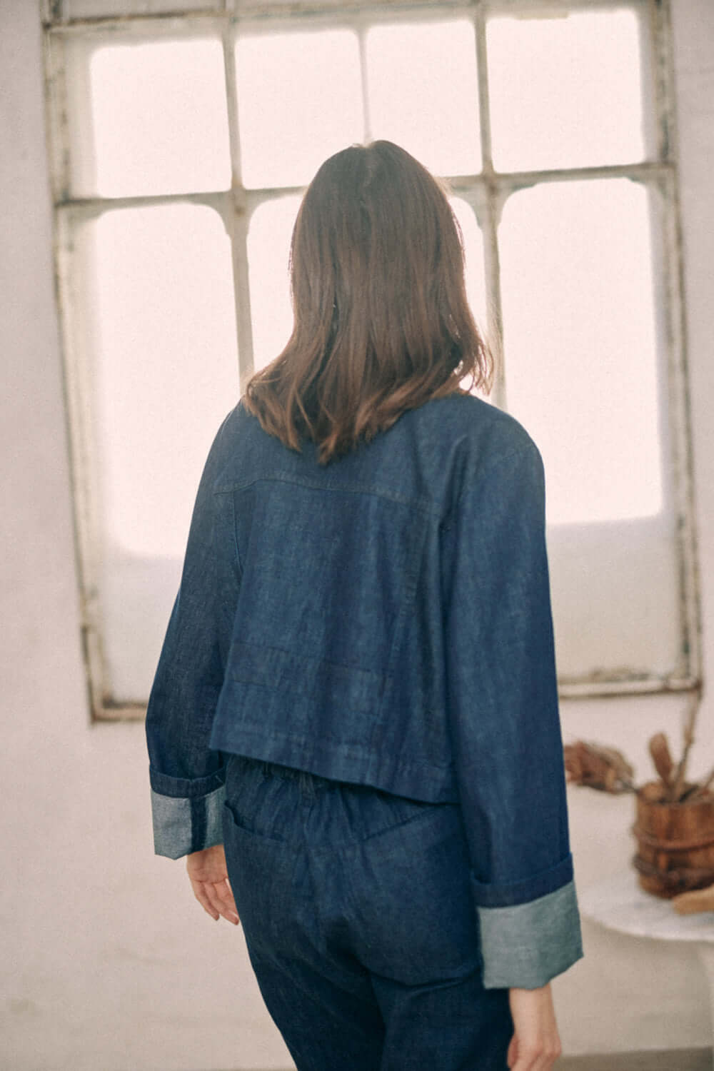 Woman wearing navy denim jacket made from 100% organic cotton, showing turned sleeves and back details. Model height 175cm, size S.