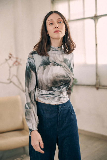 Woman wearing a printed wrap top made from 100% Ecovero viscose, styled with high-waisted jeans in a room with natural lighting.