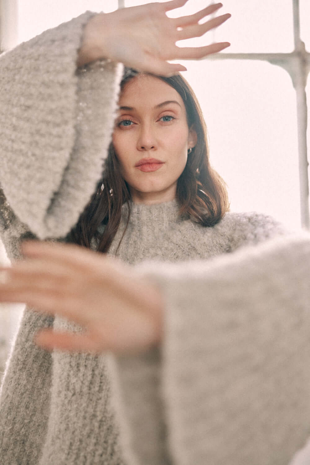 Woman wearing a grey wool tunic sweater made of alpaca and recycled polyester yarn, soft texture with flared sleeves.