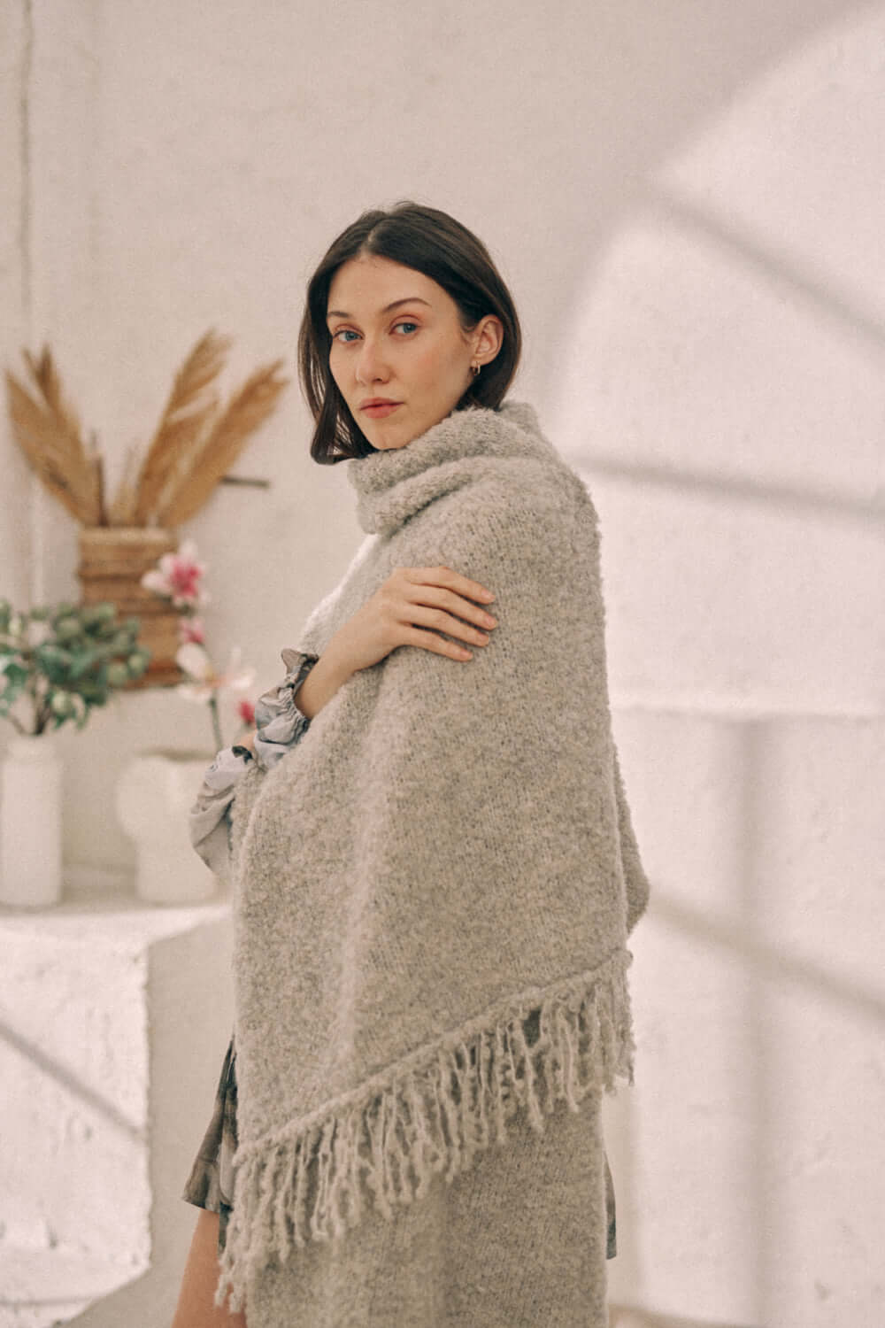 Woman wearing a versatile grey poncho scarf made from sustainable alpaca and recycled polyester yarn with fringe detailing.