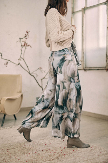 Woman wearing printed wide trousers in autumn Ecovero viscose, showcasing versatile style with separate belt in a cozy room setting.